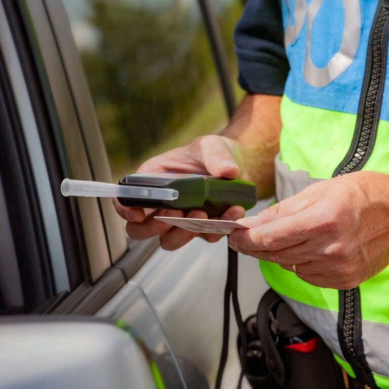 Policeman holding device for checking alcohol intoxication while standing near the stopped car